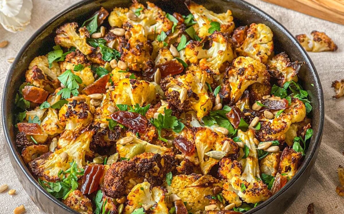 a picture of a bowl of roasted cauliflower salad with dates and tahini served with sunflower seeds for vegan warm salad recipes