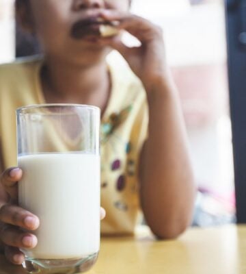 Photo shows a young school-aged child drinking milk and eating a sandwich