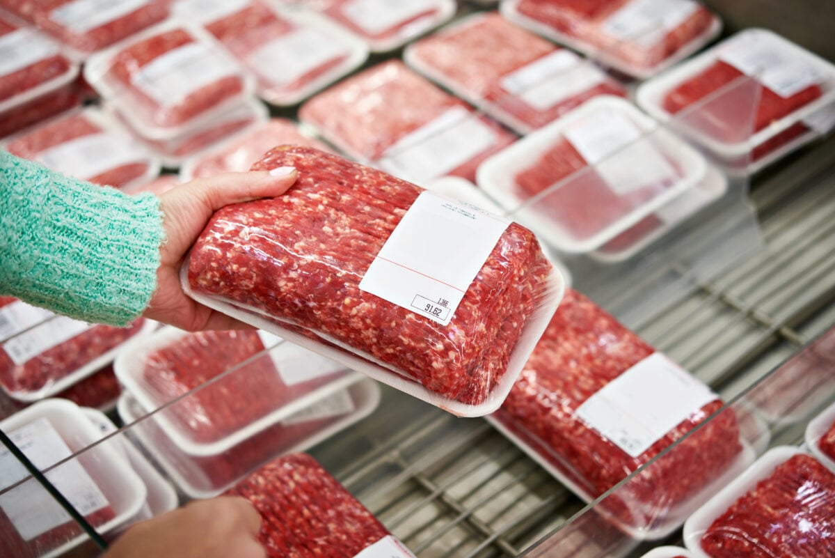 Photo shows a woman's hand as she picks up an unlabeled packet of ground beef from a refrigerator
