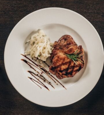 Photo shows a woman's hands holding a knife and fork next to a plate of steak and mashed potatoes