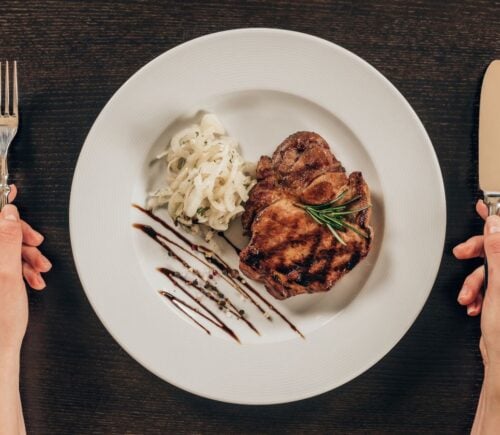 Photo shows a woman's hands holding a knife and fork next to a plate of steak and mashed potatoes