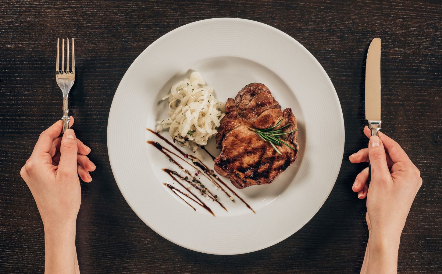 Photo shows a woman's hands holding a knife and fork next to a plate of steak and mashed potatoes