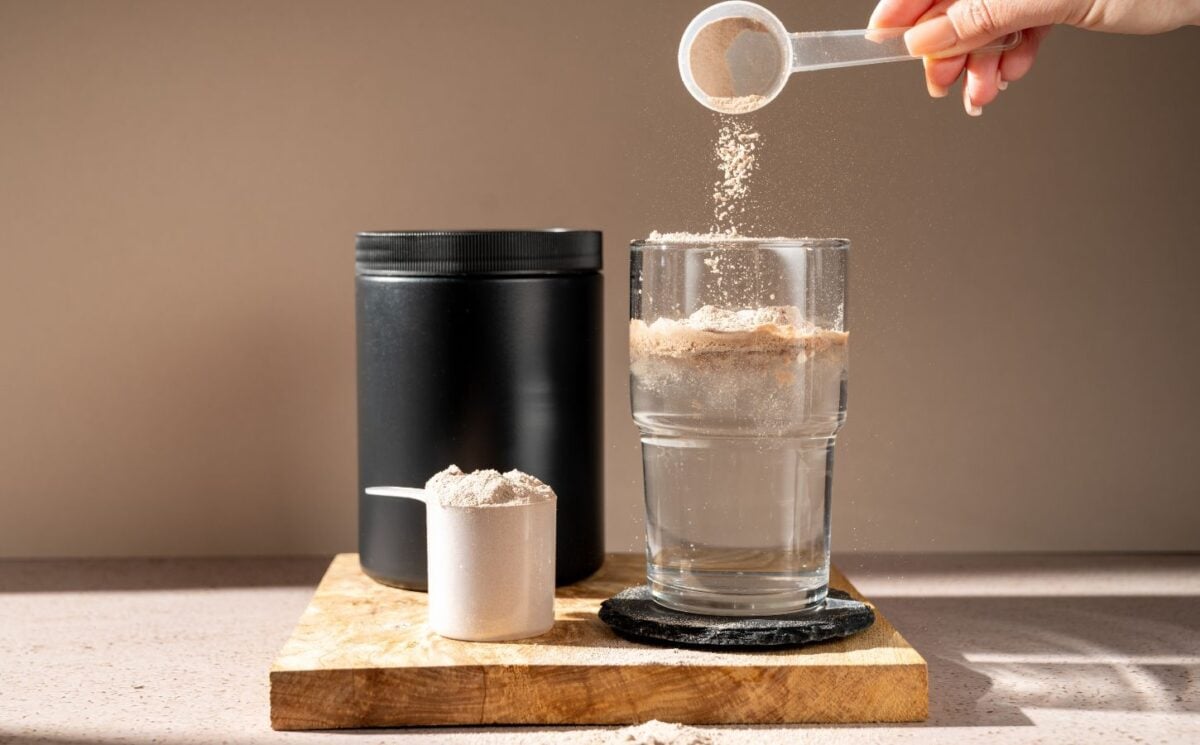A person pouring a scoop of creatine into a glass of water