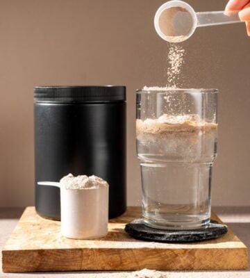 A person pouring a scoop of creatine into a glass of water