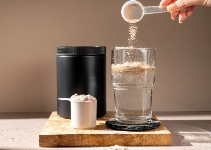 A person pouring a scoop of creatine into a glass of water