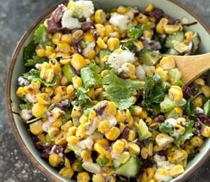 A vegan feta and corn salad in a bowl with a wooden serving spoon