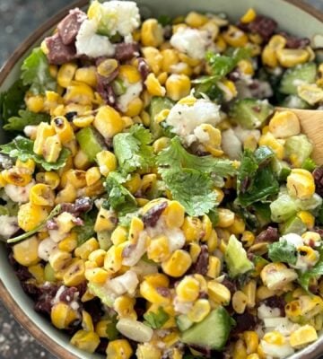 A vegan feta and corn salad in a bowl with a wooden serving spoon