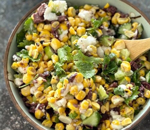 A vegan feta and corn salad in a bowl with a wooden serving spoon