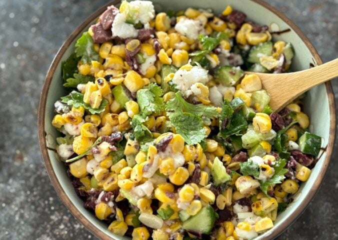 A vegan feta and corn salad in a bowl with a wooden serving spoon