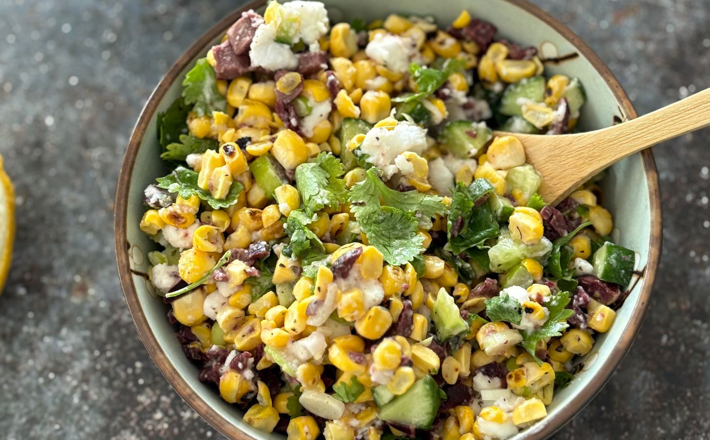 A vegan feta and corn salad in a bowl with a wooden serving spoon