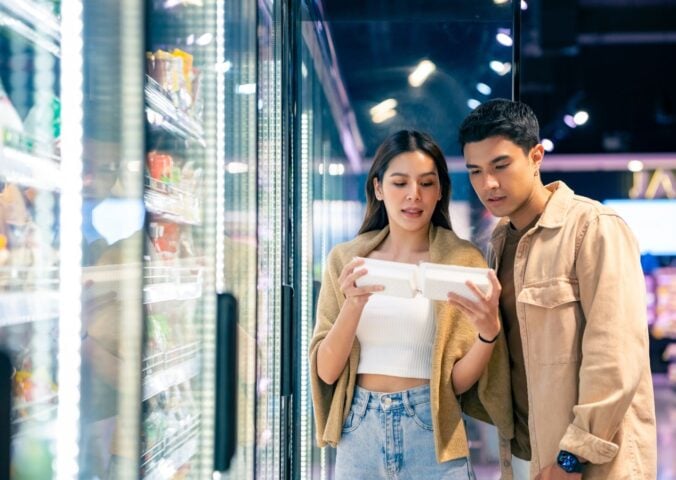 Photo shows a young couple in the supermarket reading the back of a packet together