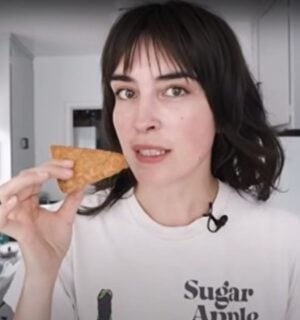 Vegan YouTuber Merle O'Neal holds a wedge of tempeh parmesan that's ready to be grated as she stands in her kitchen