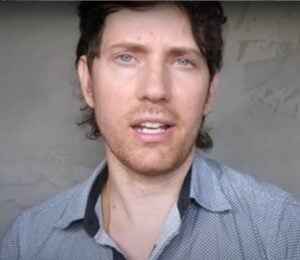 Mic the Vegan speaks to the camera in front of a grey background in a still from his video about vegan collagen