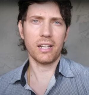 Mic the Vegan speaks to the camera in front of a grey background in a still from his video about vegan collagen