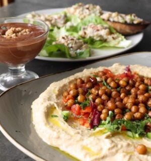 Shot of three vegan dishes made using chickpeas: hummus topped with roasted chickpeas, chickpea tuna salad, and aquafaba chocolate mousse