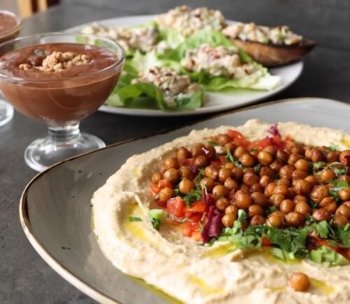Shot of three vegan dishes made using chickpeas: hummus topped with roasted chickpeas, chickpea tuna salad, and aquafaba chocolate mousse