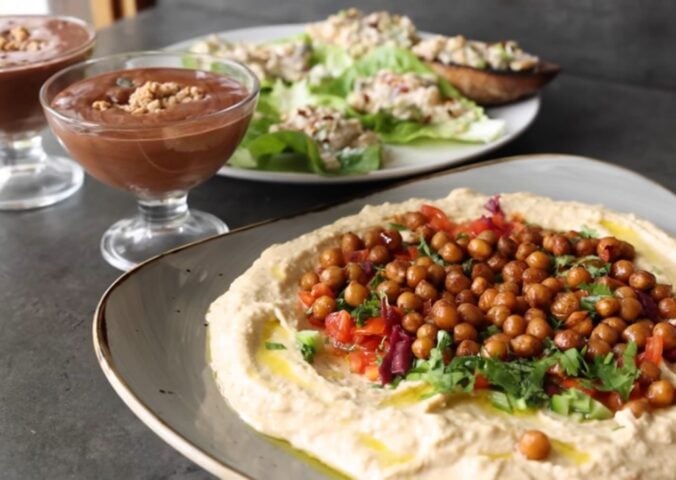 Shot of three vegan dishes made using chickpeas: hummus topped with roasted chickpeas, chickpea tuna salad, and aquafaba chocolate mousse