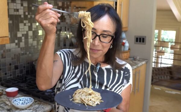 Miyoko Schinner pulls a forkful of her freshly cooked vegan cacio e pepe up from the black plate she's holding in her hand as she stands in her kitchen