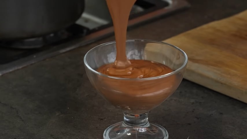 Aquafaba chocolate mousse is being poured into a clear glass dessert goblet
