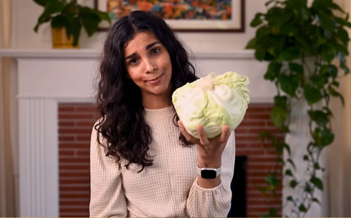 Vegan chef Nisha Vora holds a head of cabbage with a skeptical look on her face as she explores ways to overcome veggie aversion