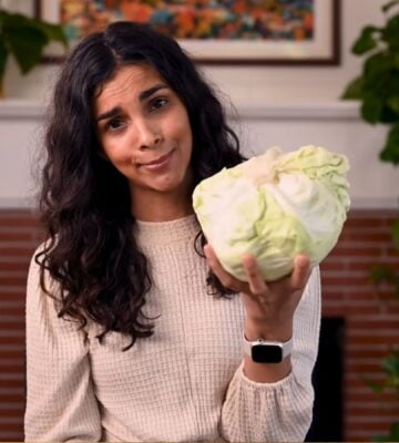 Vegan chef Nisha Vora holds a head of cabbage with a skeptical look on her face as she explores ways to overcome veggie aversion