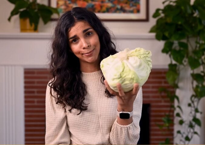 Vegan chef Nisha Vora holds a head of cabbage with a skeptical look on her face as she explores ways to overcome veggie aversion