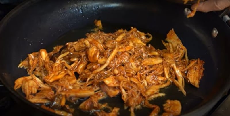 Shredded king trumpet mushrooms cooking in a skillet, coated in a smoky-sweet marinade to resemble pulled pork