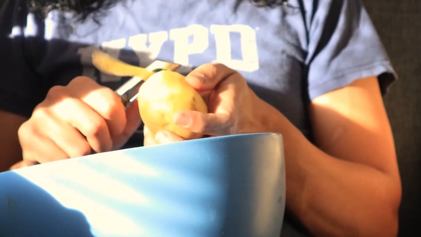 Wearing a blue NYPD t-shirt, Veganisyum peels a potato over a light blue bowl