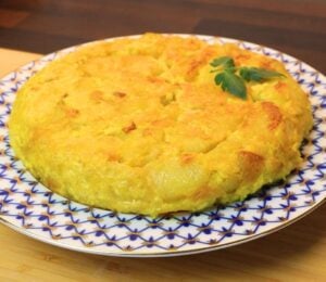 Vegan Spanish tortilla de patatas on a blue and white plate on a table, topped with tomato leaves