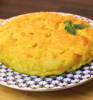 Vegan Spanish tortilla de patatas on a blue and white plate on a table, topped with tomato leaves