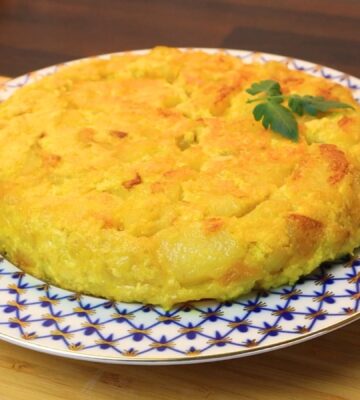 Vegan Spanish tortilla de patatas on a blue and white plate on a table, topped with tomato leaves