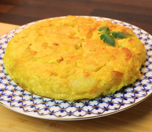 Vegan Spanish tortilla de patatas on a blue and white plate on a table, topped with tomato leaves