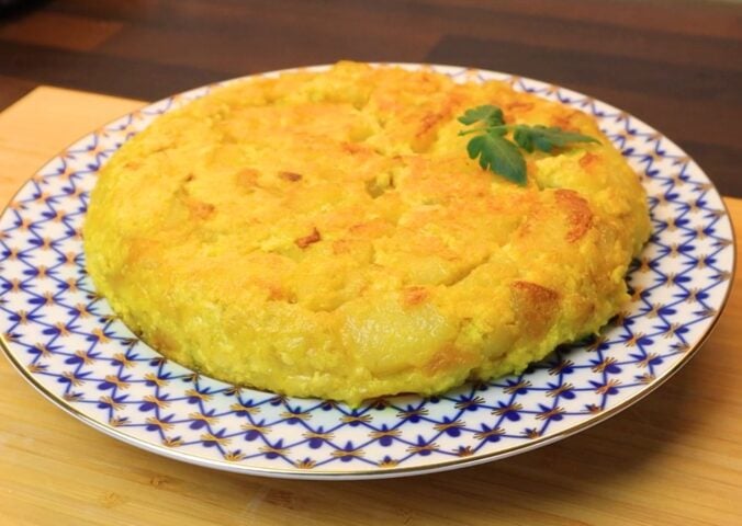 Vegan Spanish tortilla de patatas on a blue and white plate on a table, topped with tomato leaves