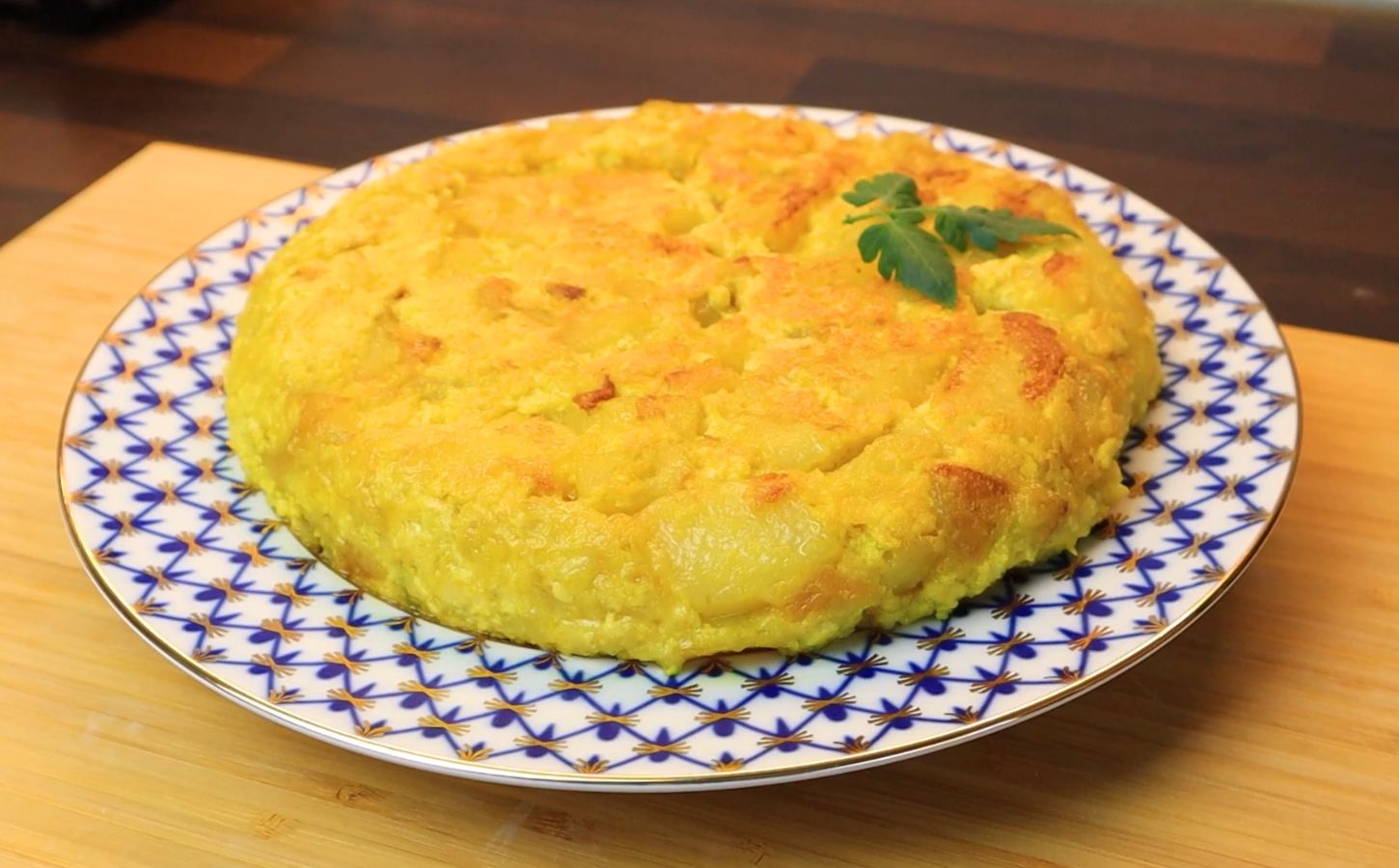Vegan Spanish tortilla de patatas on a blue and white plate on a table, topped with tomato leaves