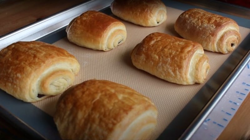 Six freshly baked chocolate croissants rest on a silicone baking mat