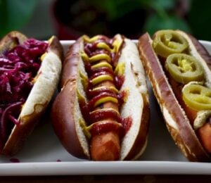 Three carrot dogs, one with red cabbage, one with ketchup and mustard, and one with jalepeno
