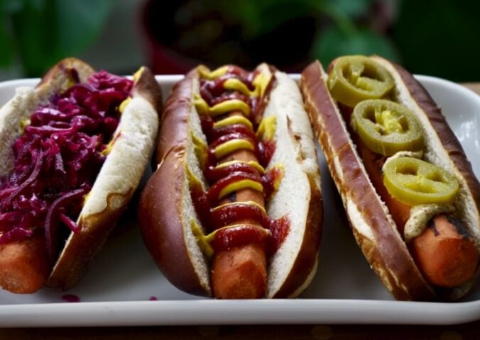 Three carrot dogs, one with red cabbage, one with ketchup and mustard, and one with jalepeno