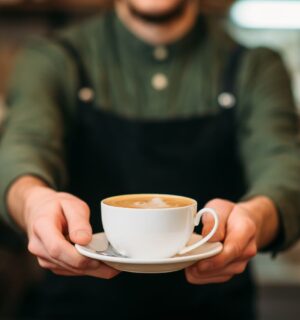 Photo shows a barista holding out a cup of coffee in a saucer
