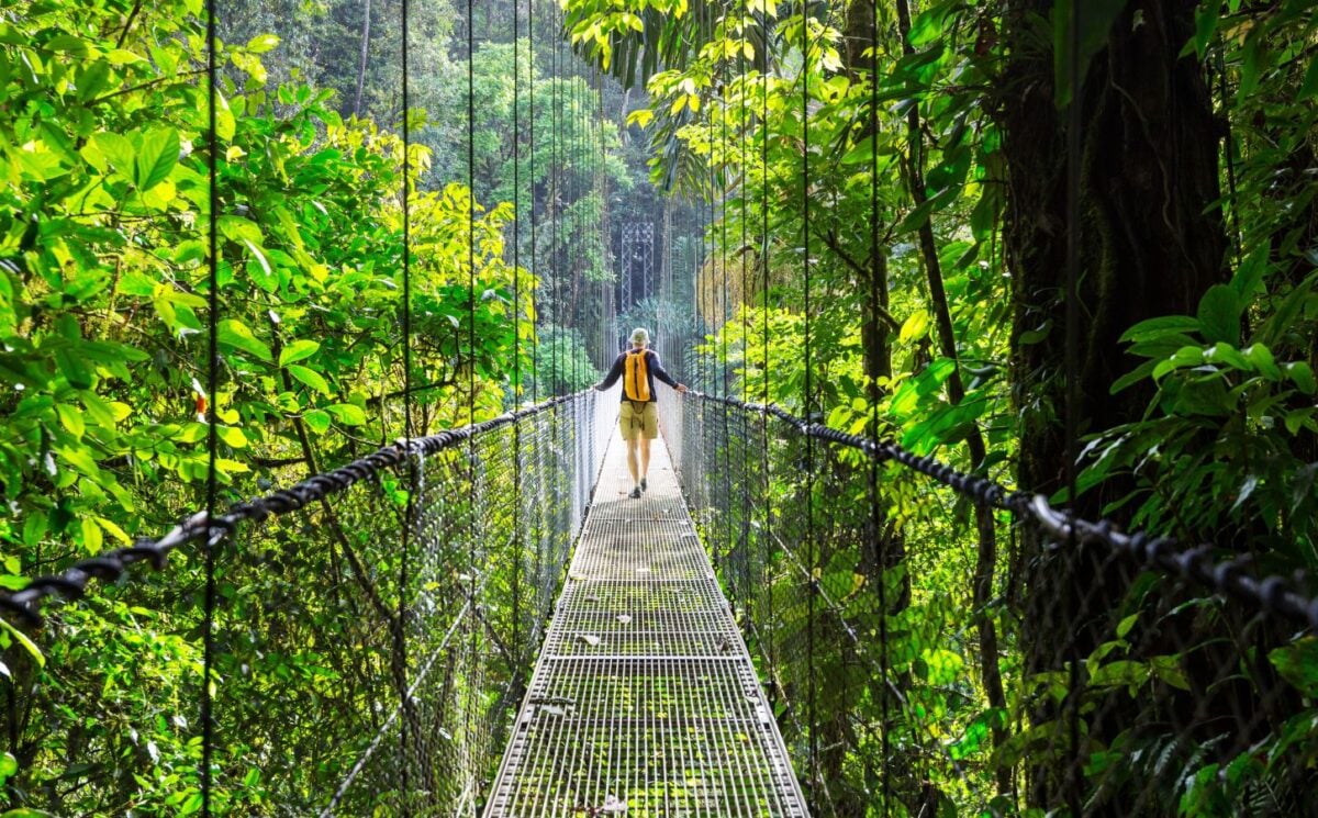 A vegan traveller walking across a bridge in Costa Rica next to lots of bright green shrubbery