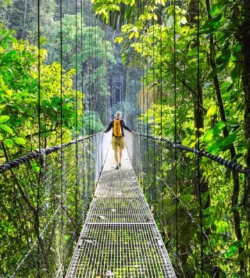 A vegan traveller walking across a bridge in Costa Rica next to lots of bright green shrubbery