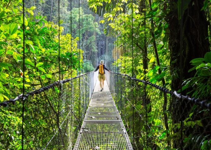 A vegan traveller walking across a bridge in Costa Rica next to lots of bright green shrubbery