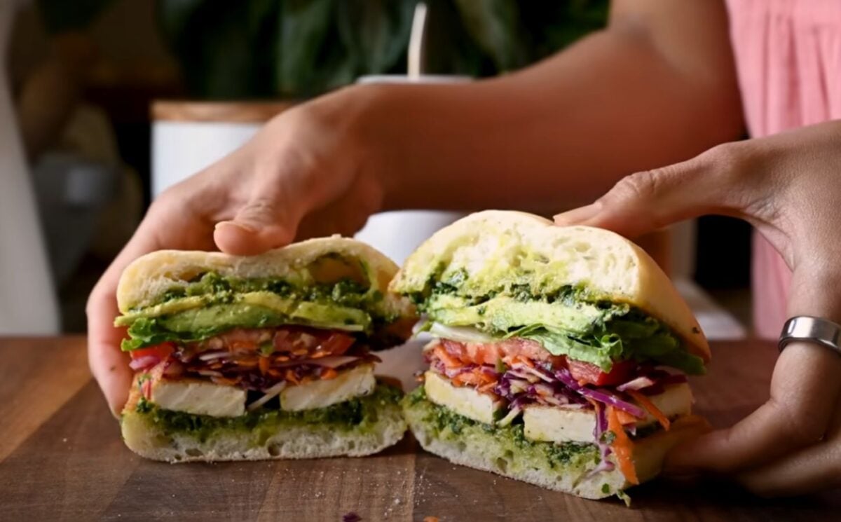 A crispy tofu sandwich filled with avocado, tomato, and other salad