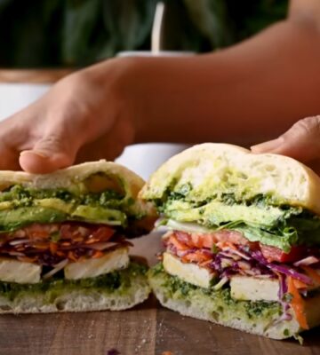 A crispy tofu sandwich filled with avocado, tomato, and other salad