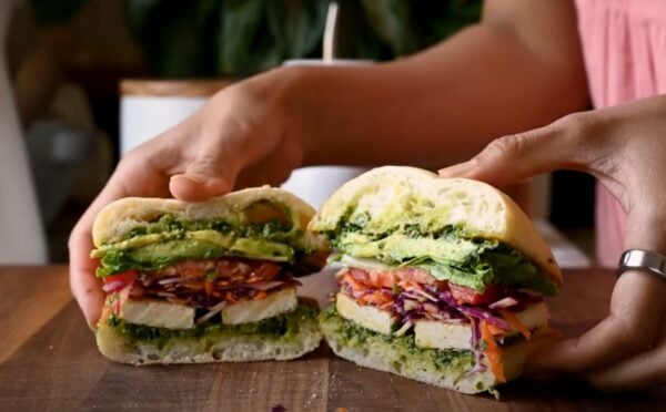 A crispy tofu sandwich filled with avocado, tomato, and other salad
