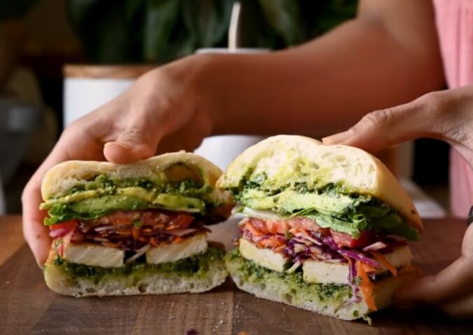 A crispy tofu sandwich filled with avocado, tomato, and other salad