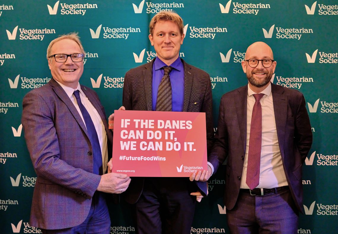 Photo shows, from left to right: Richard McIlwain, chief executive of Vegetarian Society; Rasmus Prehn, member of the Danish Parliament and former minister of Food, Agriculture and Fisheries; and Rune-Christoffer Dragsdahl, the Secretary-General at Vegetarian Society of Denmark, standing in front of a Vegetarian Society backdrop and holding a sign that reads "if the Danes can do it, we can do it"