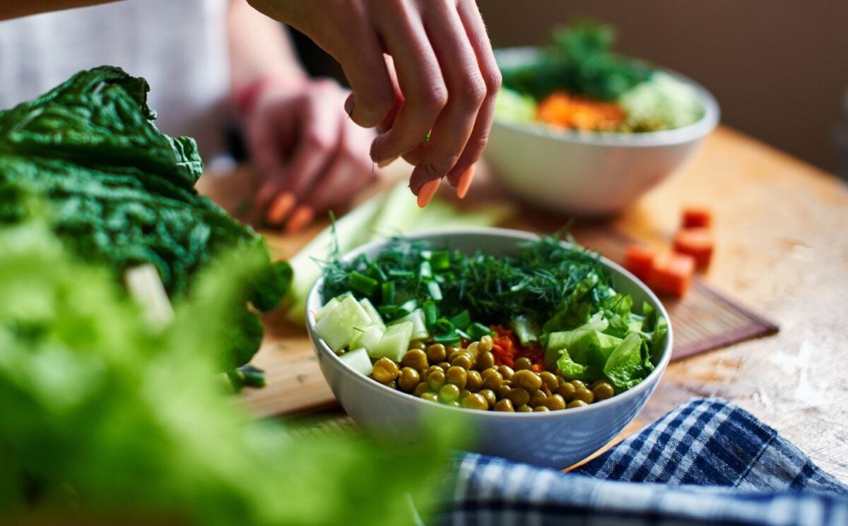 A close up of a hand making a healthy vegan salad with chickpeas and greens