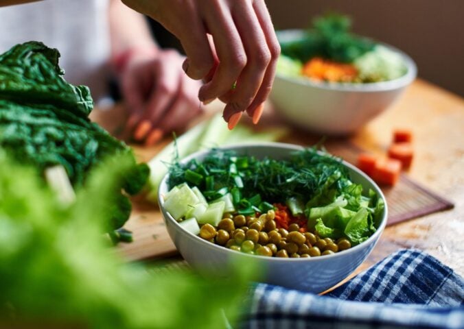 A close up of a hand making a healthy vegan salad with chickpeas and greens