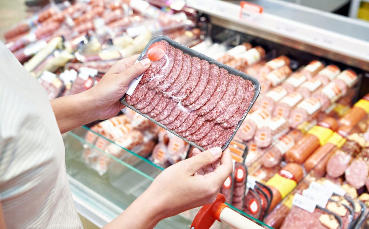 Photo shows someone holding up a package of highly processed red meat slices in the supermarket