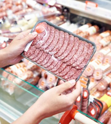 Photo shows someone holding up a package of highly processed red meat slices in the supermarket